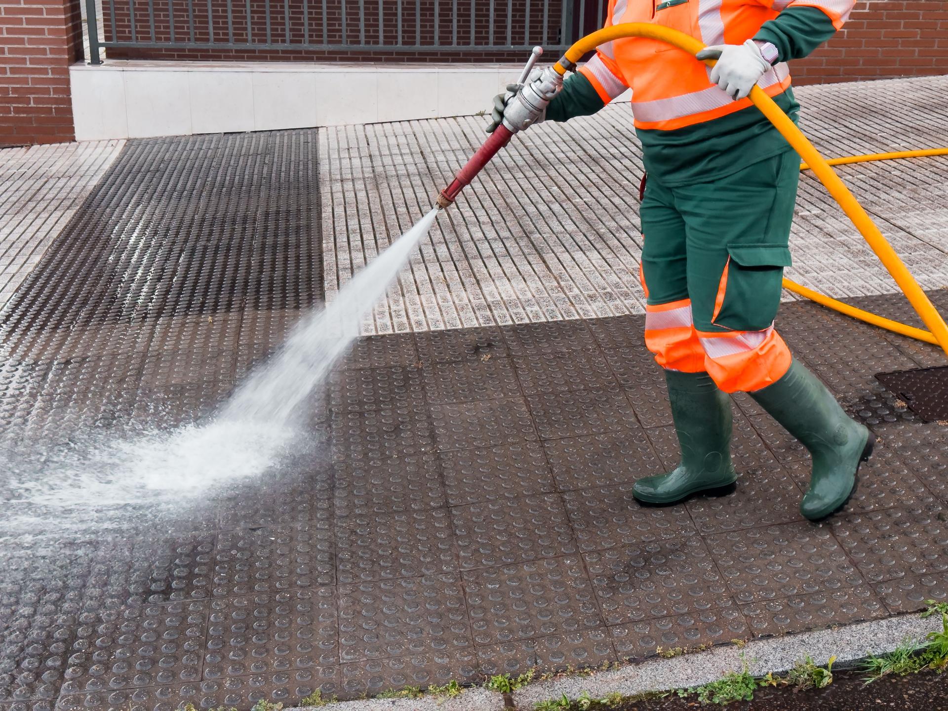 Worker power washing urban sidewalk with hose and safety gear